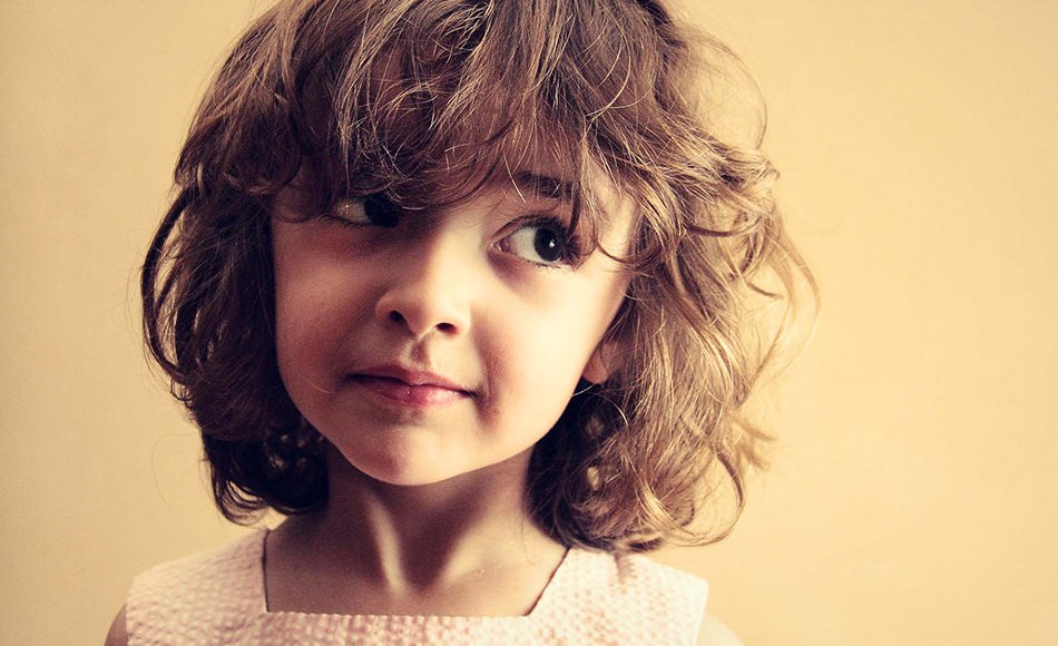 Хитрая девочка с озорным выражением лица смотрит в сторону, будто что-то задумала или скрывает. Настроение — между игрой и тайной.
