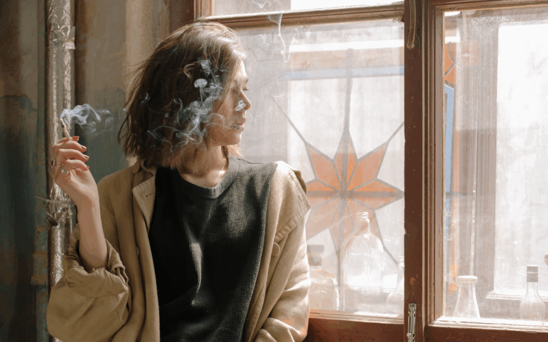 Девушка с тонким силуэтом задумчиво курит у открытого окна